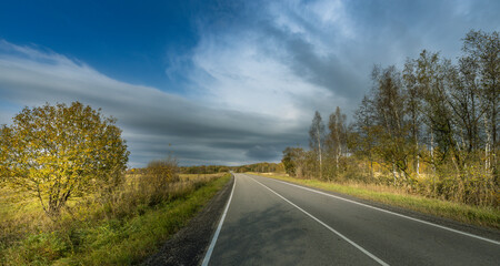 A road with trees in the background and a cloudy sky