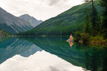 a girl meditates on the shore of a mountain lake in Altai