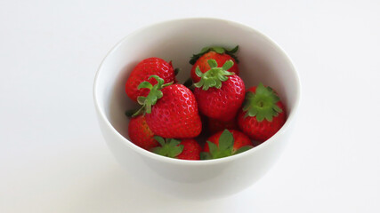 A white bowl full of red ripe fresh strawberries