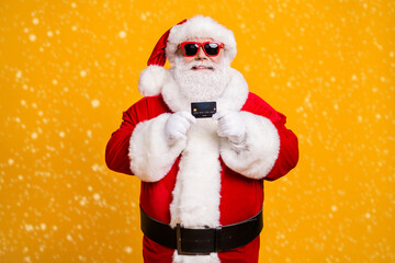 Portrait of his he nice attractive cheerful cheery Santa holding in hand bank card spend budget safe shopping isolated bright vivid shine vibrant yellow color background