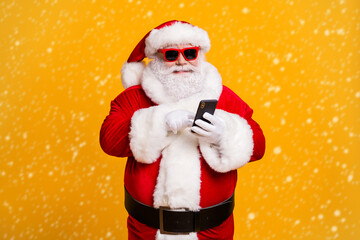 Portrait of his he nice attractive cheerful focused Santa using device gadget chatting app 5g web service shopping order blogging isolated bright vivid shine vibrant yellow color background