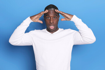 Surprised man in white sweater with hands on head..