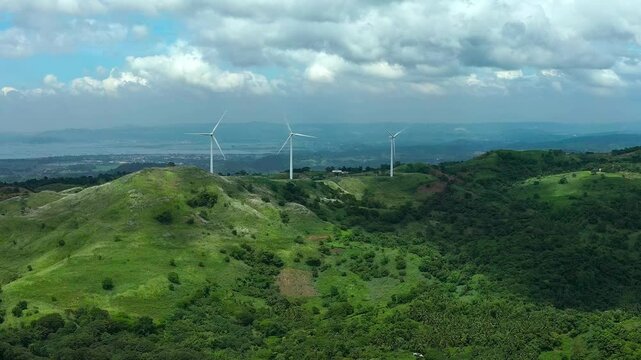 Pililla Wind Mills between green mountains of Philippines Rizal. Cloudy day on asian island. Production of eco friendly energy with wind. Drone wide shot.
