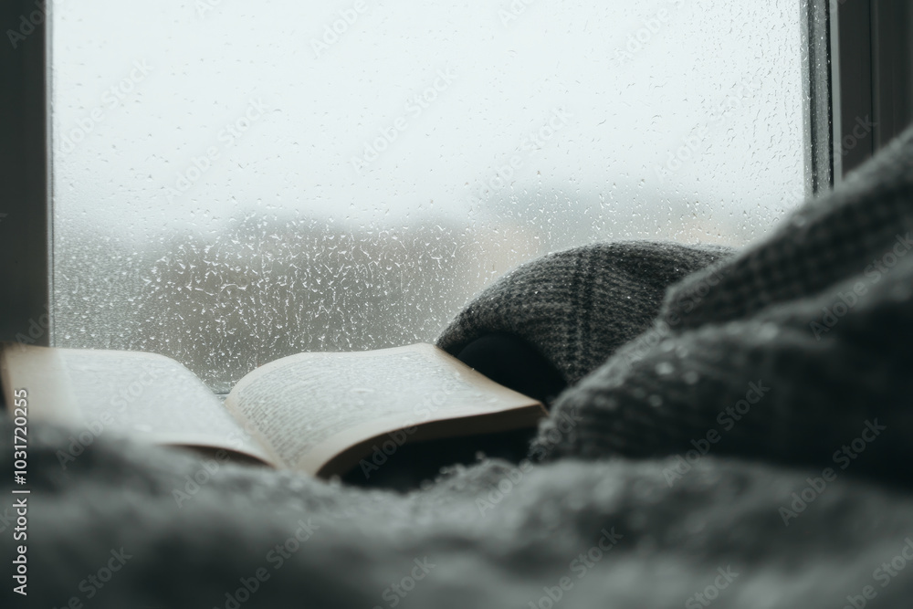 Poster a book is open on a bed with a blanket and a window behind it