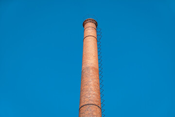 Chaminé industrial histórica em tijolos vermelhos com umas escadas de acesso ao alto, sob um céu azul