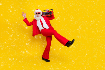 Full length photo of excited funky santa dressed red suit tie walking enjoying boom box music empty space isolated yellow color background © deagreez
