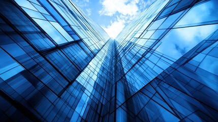 Fototapeta premium A low angle view of a glass skyscraper reaching up to a bright blue sky with clouds.