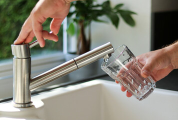 Close up of male hands pouring tap water into a glass in the kitchen
