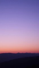 Fototapeta premium purple and blue sky with a lone airplane flying over the mountains