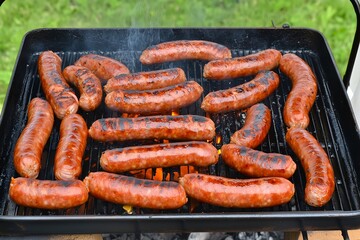 Fototapeta premium Grilled sausages sizzling on barbecue grill outdoors