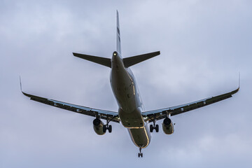 An airplane flies through a cloudy sky with a red tail light