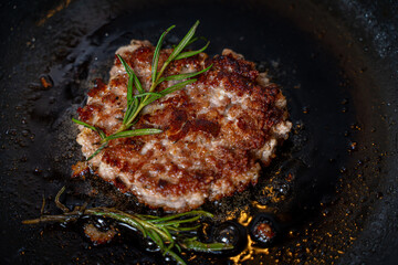 Beef cutlet with rosemary sprigs in a pan. A burger patty is fried on a black background. High quality photo