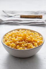 A shiny metal bowl, viewed from the front, is filled with uncooked  pasta 'ditalini'.
