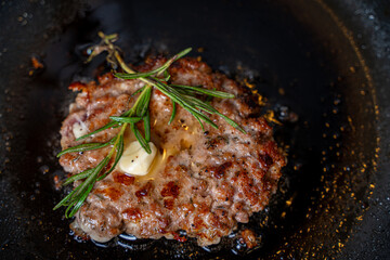 Beef cutlet with rosemary sprigs in a pan. A burger patty is fried on a black background. High quality photo