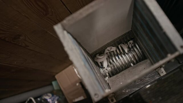 Top closeup of hand of anonymous dark-skinned male labourer throwing white polyethylene plastic beverage bottle caps into grinder for shredding into pellets at recycling plant