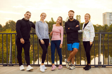Portrait of a group of young athletic people on a city bridge. Happy smiling friends after training. Sports lifestyle concept. Preparing colleagues for the city marathon, challenge