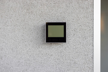 Electronic thermostat mounted on white wall displaying current indoor temperature. Device is sleek, modern, and essential for climate control in a minimalist environment.