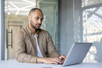 Professional man using laptop in office setting, showing concentration on work tasks. Modern...