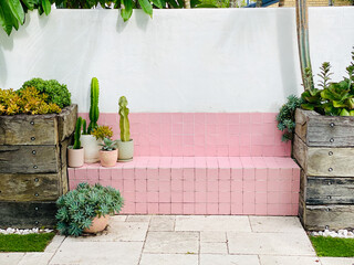Charming pink tile bench surrounded by potted succulents and cacti in a minimal outdoor garden...