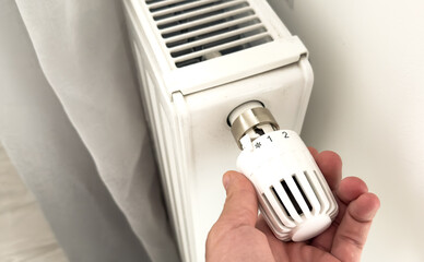 A hand adjusts the temperature on a radiator thermostat, marking the start of the heating season.