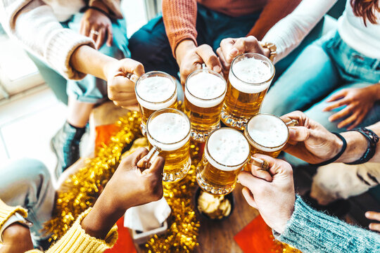 Happy people wearing winter clothes toasting beer glasses at brewery pub table - Festive friends celebrating winter holidays sitting at bar restaurant - Food and beverage concept
