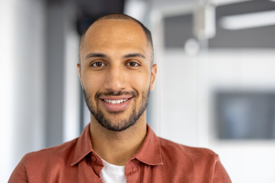 Confident business professional wearing casual orange shirt in modern office setting exuding warmth with genuine smile. Perfect image for themes of professionalism, approachability, and positivity.