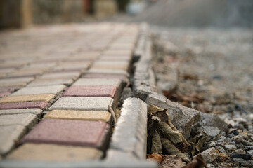 The view focuses on cracked pavement and misaligned brick tiles, scattered with dried leaves, illustrating the deterioration of a once well-maintained walkway.