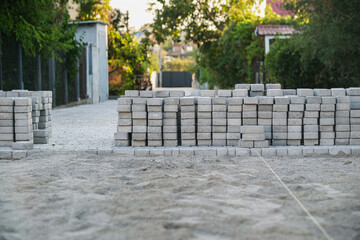 Workers are preparing to build a new path by carefully arranging gray bricks along a serene street,...