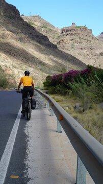 Mountain bike rider. Cyclist enters mountain road after short stop. The tourist cyclist on mountain bike equipped with bags wears helmet and yellow jersey. Vertical video
