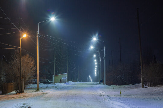 Evening village street illuminated by lampposts. Barancha, Ural, 2023.