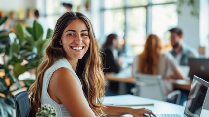 A smiling woman sitting at an office desk with her team in the background