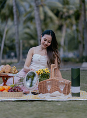 Smiling pretty asian woman in white dress having a summer picnic in a beautiful green garden. Leisure and people concept.