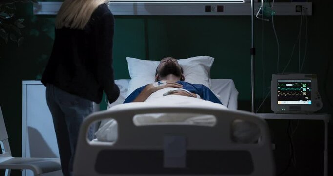 Exhausted tired young woman enters the hospital ward of his husband sits and supports while man in coma .