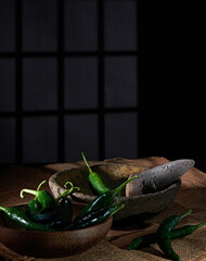 large green chilies in a stone mortar, prepared to be ground into a spicy chili sauce, photographed against a dark background