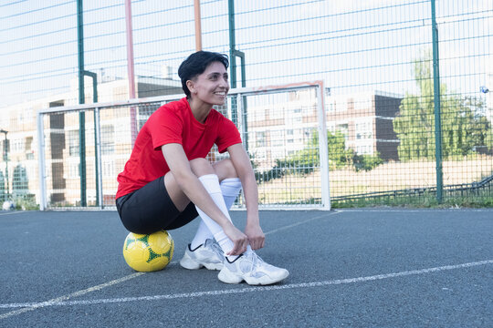 United Kingdom, Female football player sitting on ball and tying shoe - Powered by Adobe