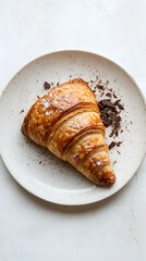 Chocolate croissant on a white plate, viewed from above, showcasing its flaky layers and rich filling, inviting and appetizing presentation