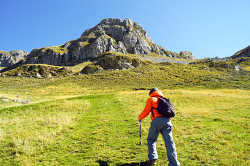 A tourist begins his ascent to the top: a man with a backpack walks along the mountainside using...