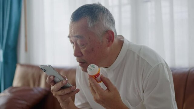 Asian senior man use smart Phone research,reading label and learning of medicine,telehealth services at home.Online patient with pills bottle,tablet and mobile for information or health benefits