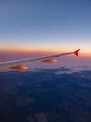 Serene view from an airplane window at sunset, showcasing the plane wing and vibrant colors of the sky, perfect for travel and aviation themes