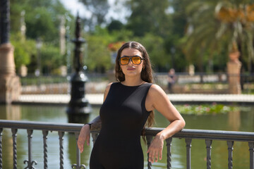 Young woman, brunette, beautiful, very tattooed, with black overalls and glasses with orange...