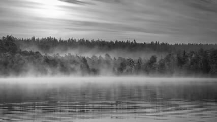 Fototapeta premium Sunrise with fog forming over a lake in Sweden, at dawn in black and white.