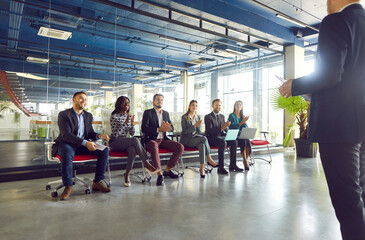 Various businessmen listen to male business leader during training lecture or corporate meeting. Group of happy diverse entrepreneurs applauding on a seminar in board room in modern business center. 