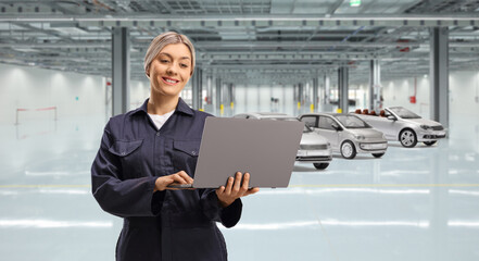 Fototapeta premium Female worker in a uniform holding a laptop computer in a garage