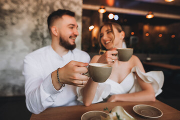 Newlyweds couple in love sitting in a cafe, hugging, touching each other with their hands. Wedding day, celebration, restaurant, coffee shop. The bride and groom drink coffee.