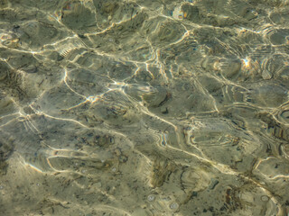 Crystal clear transparent water with fine white sand base with bright reflection of sun in water movement. Lines and shapes in nature