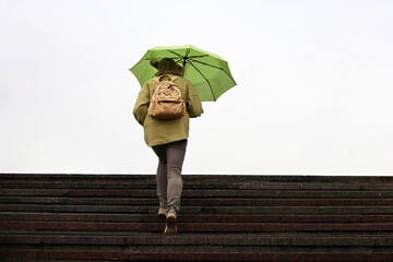 Woman with green umbrella walking up the stone steps. Rain in autumn city