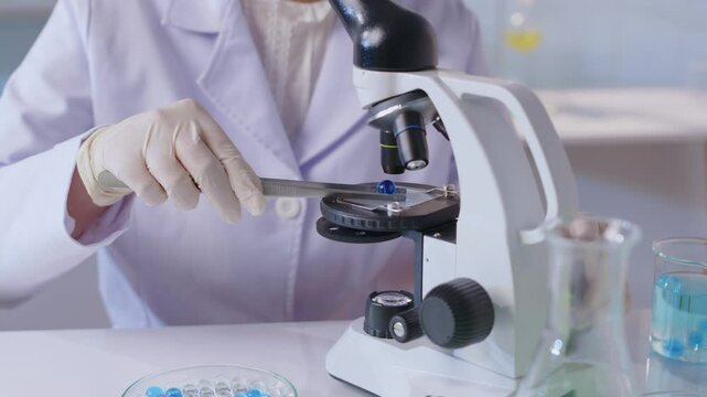High-quality video sample of a chemist gently adjusting the level and picking up a blue hydrogel ball and placing it on the microscope surface for observation in a modern laboratory setting.