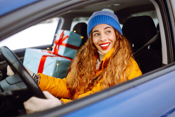 Cheerful woman driving and smiling with christmas presents in the car looking happy during the...