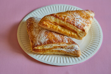 Triangles of puff pastry with sugar sprinkle on a disposable plate on a pink background, fast food, street food.