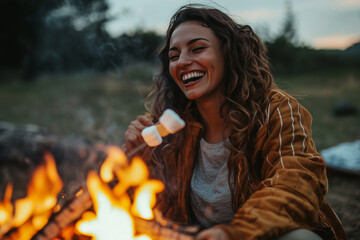 A woman is sitting by a fire, eating marshmallows